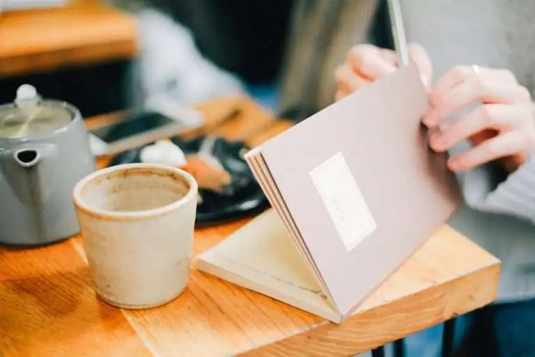 person opening a book with a empty coffee cup next to it