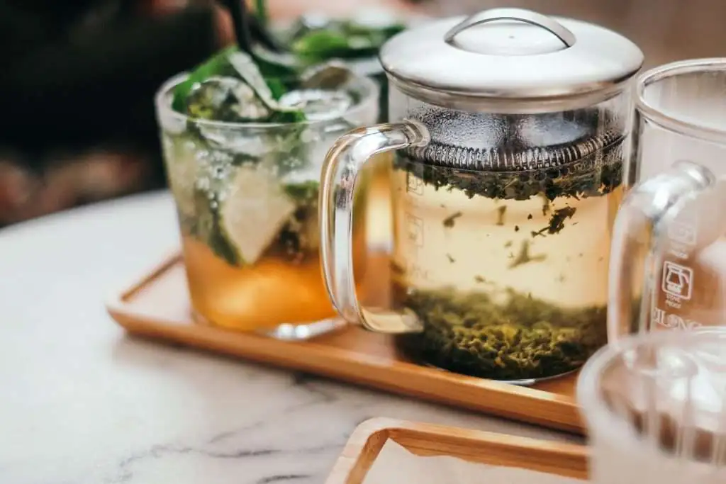 tea in a glass teapot with teacups surrounding it