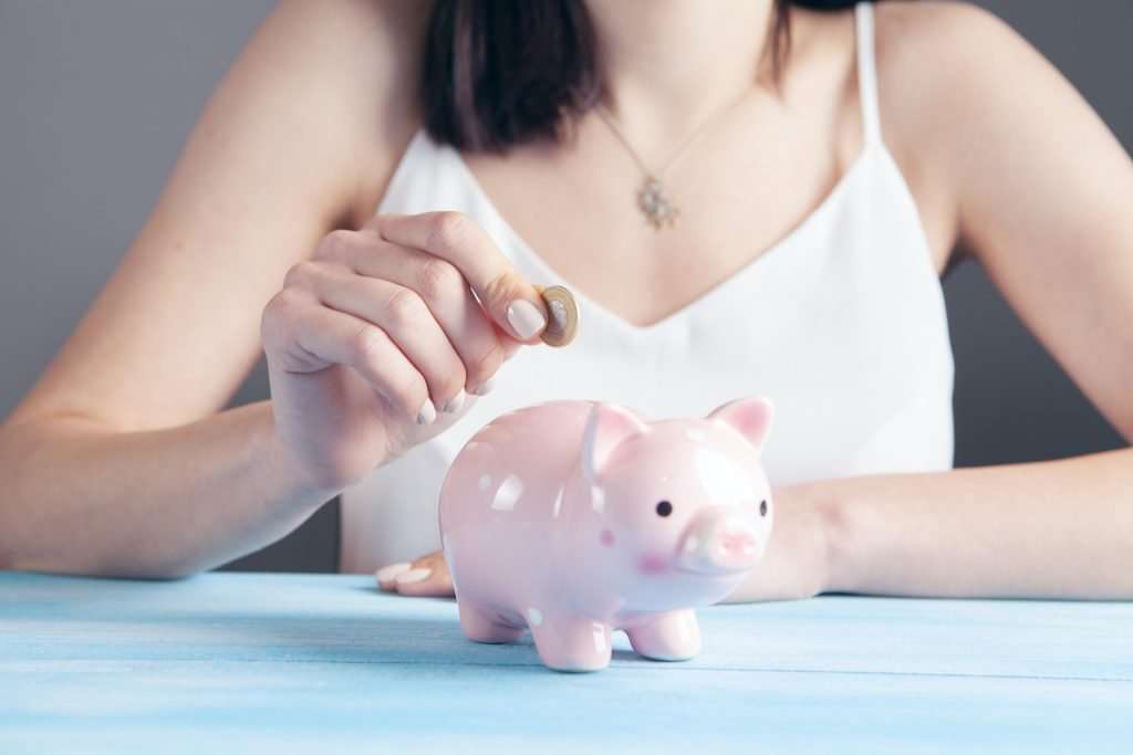 women placing a coin in a piggy bank